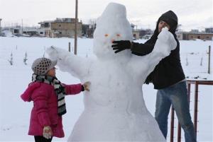 A Syrian man and his daughter make a snowman at a refugee camp in Lebanon.